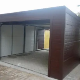 Nowoczesny garaż blaszany w brązowym odcieniu z częściowo otwartą bramą segmentową i bocznymi drzwiami, widok z zewnątrz na kostce brukowej.