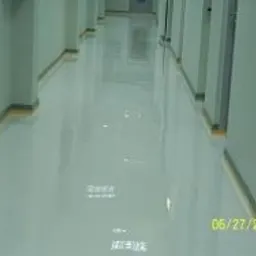 Błyszcząca, jasna posadzka przemysłowa w korytarzu, widoczne odbicia światła na powierzchni, ściany pomalowane na jasnozielono, data 06/27/2009 w prawym dolnym rogu.