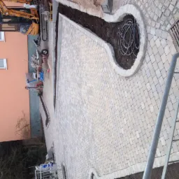 Ułożona kostka brukowa na posesji z wyznaczonymi miejscami na zieleń, widoczny mini-koparka i narzędzia budowlane w tle.