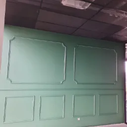 Ściana wykończona zielonymi panelami dekoracyjnymi z ramkami, widoczne elementy instalacji pod sufitem podwieszanym.