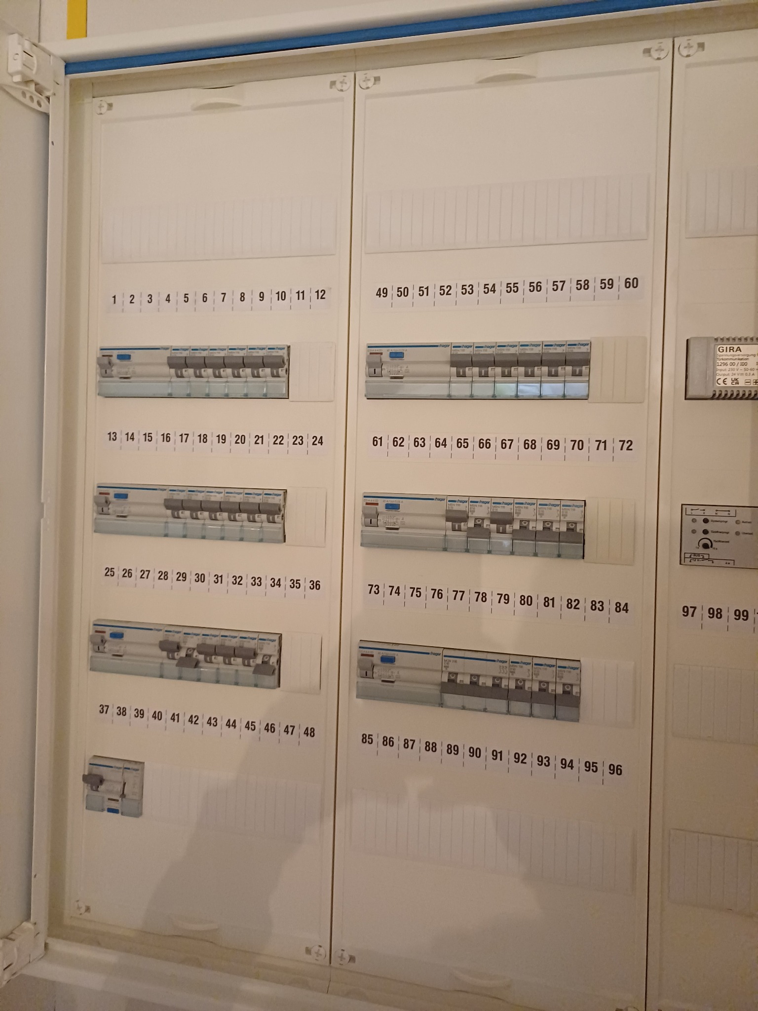 Rozdzielnica elektryczna z ponumerowanymi bezpiecznikami, widok z bliska na białą obudowę i włączniki.