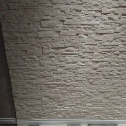 Ściana wykończona dekoracyjnym panelem imitującym kamień w odcieniach beżu w Środzie Śląskiej, z widoczną białą listwą przypodłogową i fragmentem podłogi z płytek w romby.