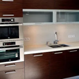 Nowoczesna kuchnia z zabudową z ciemnego drewna z poziomym usłojeniem, jasnym blatem i białymi szafkami wiszącymi z mlecznym szkłem, wyposażona w piekarnik i płytę grzewczą marki Teka.