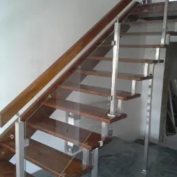 Nowoczesne schody z drewnianymi stopniami, szklaną balustradą i metalowymi słupkami, widoczne z dołu pod kątem.