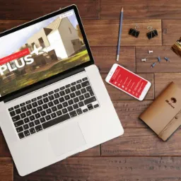 Laptop wyświetlający stronę internetową firmy z Gorzyc Wielkich, obok telefon z otwartą aplikacją, notatnik, zdjęcie budynku i przybory biurowe na drewnianym biurku.