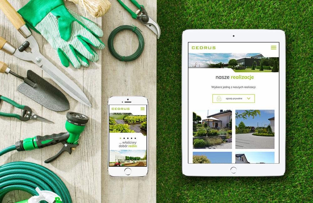 Tablet i smartfon prezentujące stronę internetową firmy ogrodniczej Cedrus, obok narzędzia ogrodnicze na drewnianym tle i trawie.