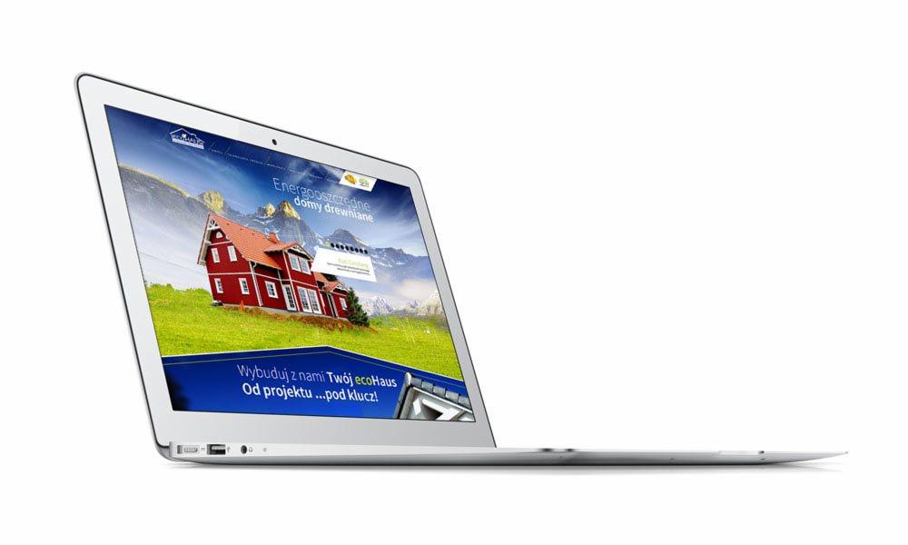 Laptop wyświetla stronę internetową z wizualizacją energooszczędnego domu drewnianego na tle gór, z hasłem 'Wybuduj z nami Twój ecoHaus. Od projektu...pod klucz!'