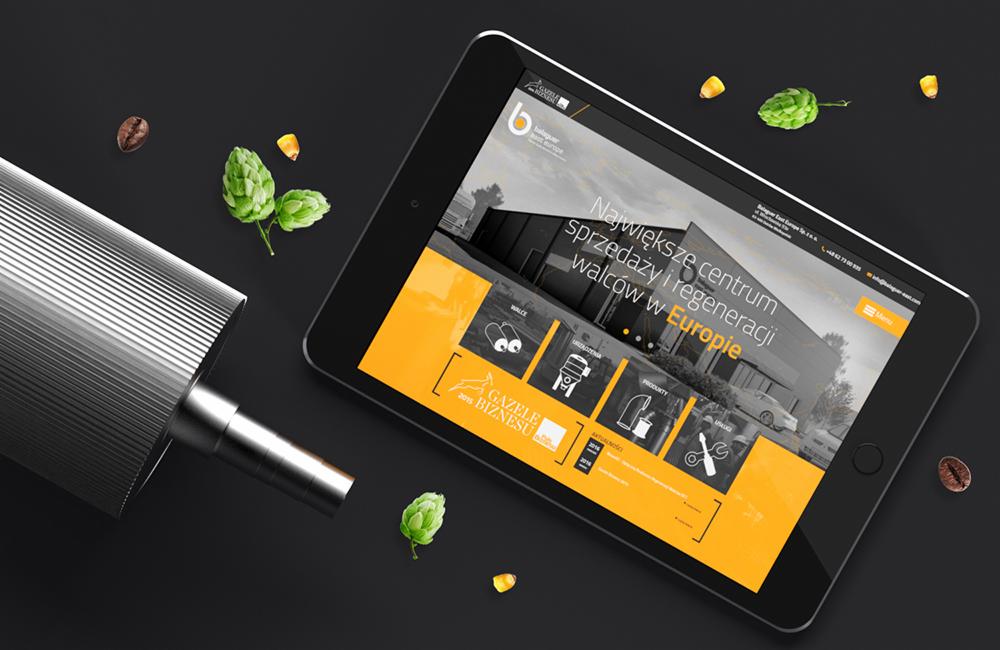 Tablet wyświetlający stronę internetową firmy zajmującej się sprzedażą i regeneracją walców, obok leży metalowy walec, szyszki chmielu, ziarna kawy i kukurydzy na ciemnym tle.