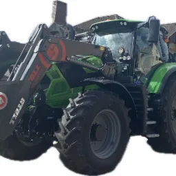 Zielony ciągnik Deutz-Fahr z ładowaczem czołowym Stoll i przyczepą rolniczą, zaparkowany na tle zabudowań mieszkalnych.