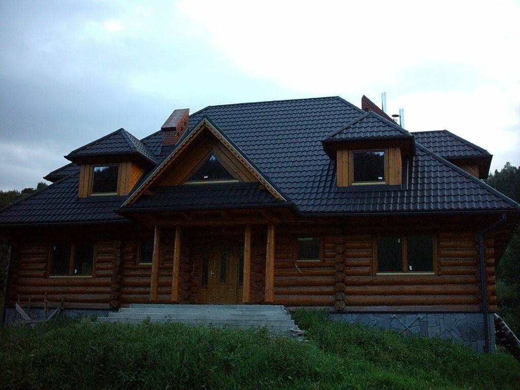 Gotowy dom z bali w Kluszkowcach z ciemnym, wielospadowym dachem z blachodachówki, widoczne schody wejściowe i otoczenie z zielenią.