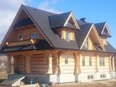 Dwukondygnacyjny dom z bali w stylu góralskim z ciemnym dachem, widoczne schody wejściowe i fragment terenu w trakcie zagospodarowywania.