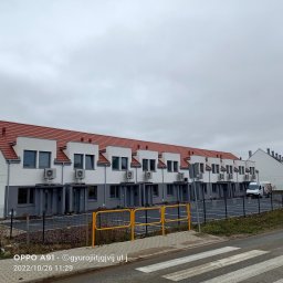 Jakub Lipka - Szereg identycznych, dwukondygnacyjnych domów z czerwoną dachówką i klimatyzacją na elewacji, widzianych z perspektywy ulicy w pochmurny dzień.