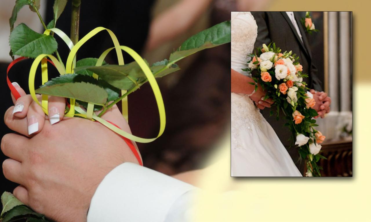 Dłonie pary młodej trzymające różę z żółtymi i czerwonymi wstążkami, w tle panna młoda z bukietem ślubnym w odcieniach bieli i brzoskwini oraz pan młody w ciemnym garniturze.