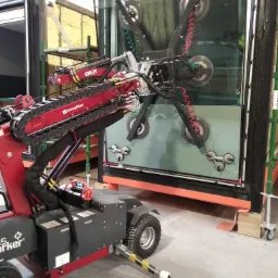 Czerwony robot podnośnik GW625 z przyssawkami mocujący dużą szybę w ramie okiennej, widoczne detale konstrukcyjne ramy i przyssawki.