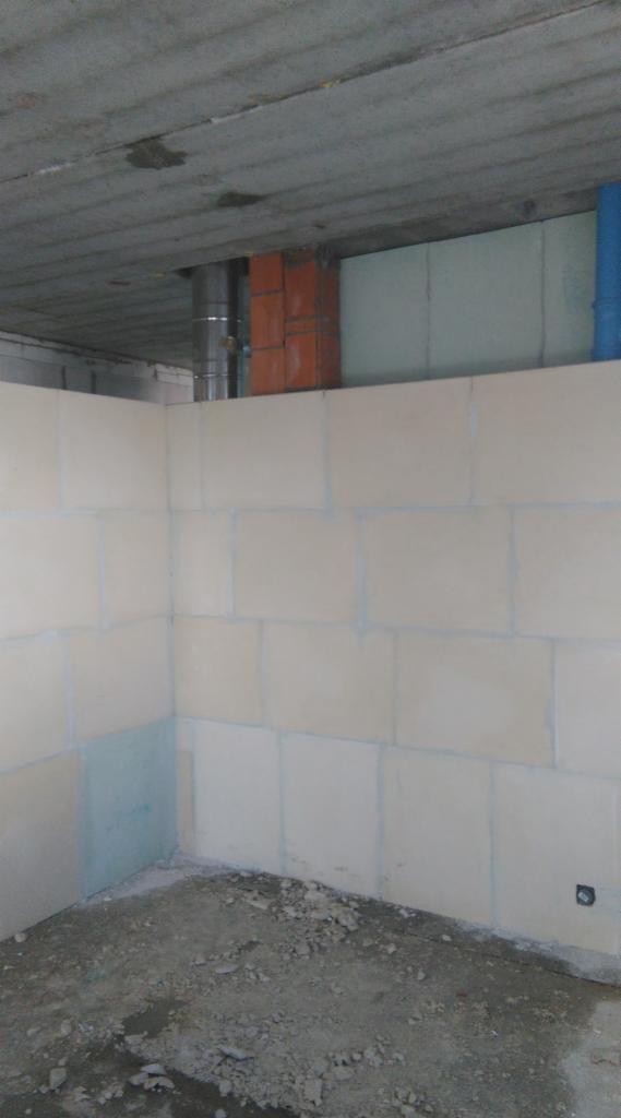 Wnętrze surowego pomieszczenia w trakcie budowy, ściany z bloczków, surowy betonowy strop, wystający komin z cegły i rura wentylacyjna, podłoga w stanie nieukończonym.