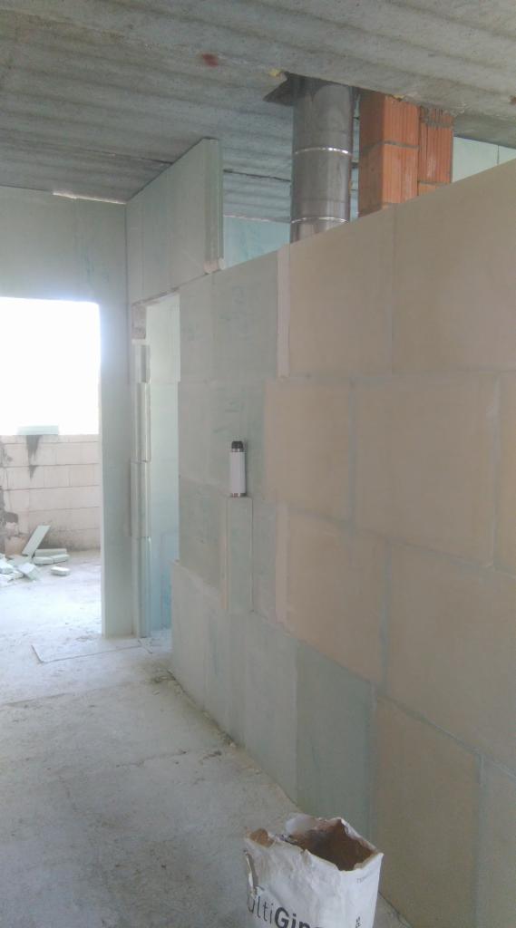 Wnętrze budynku w trakcie wznoszenia ścian z bloczków, widoczny komin, fragment okna oraz worek zaprawy murarskiej.