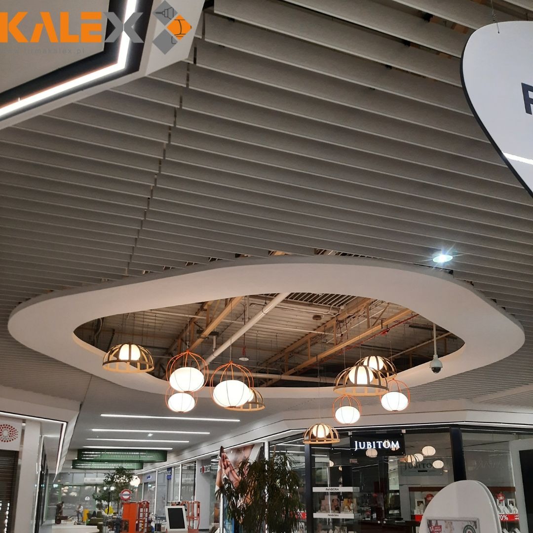 Dekoracyjny sufit rastrowy z okrągłym wycięciem i wiszącymi lampami w centrum handlowym, widok z dołu.
