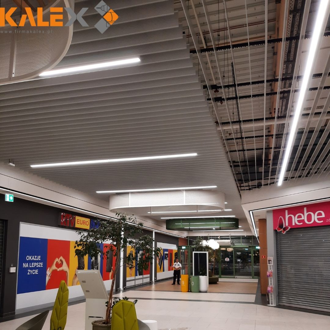 Sufit rastrowy z oświetleniem liniowym w galerii handlowej w Konopnicy, widoczny fragment instalacji nad sufitem podwieszanym.