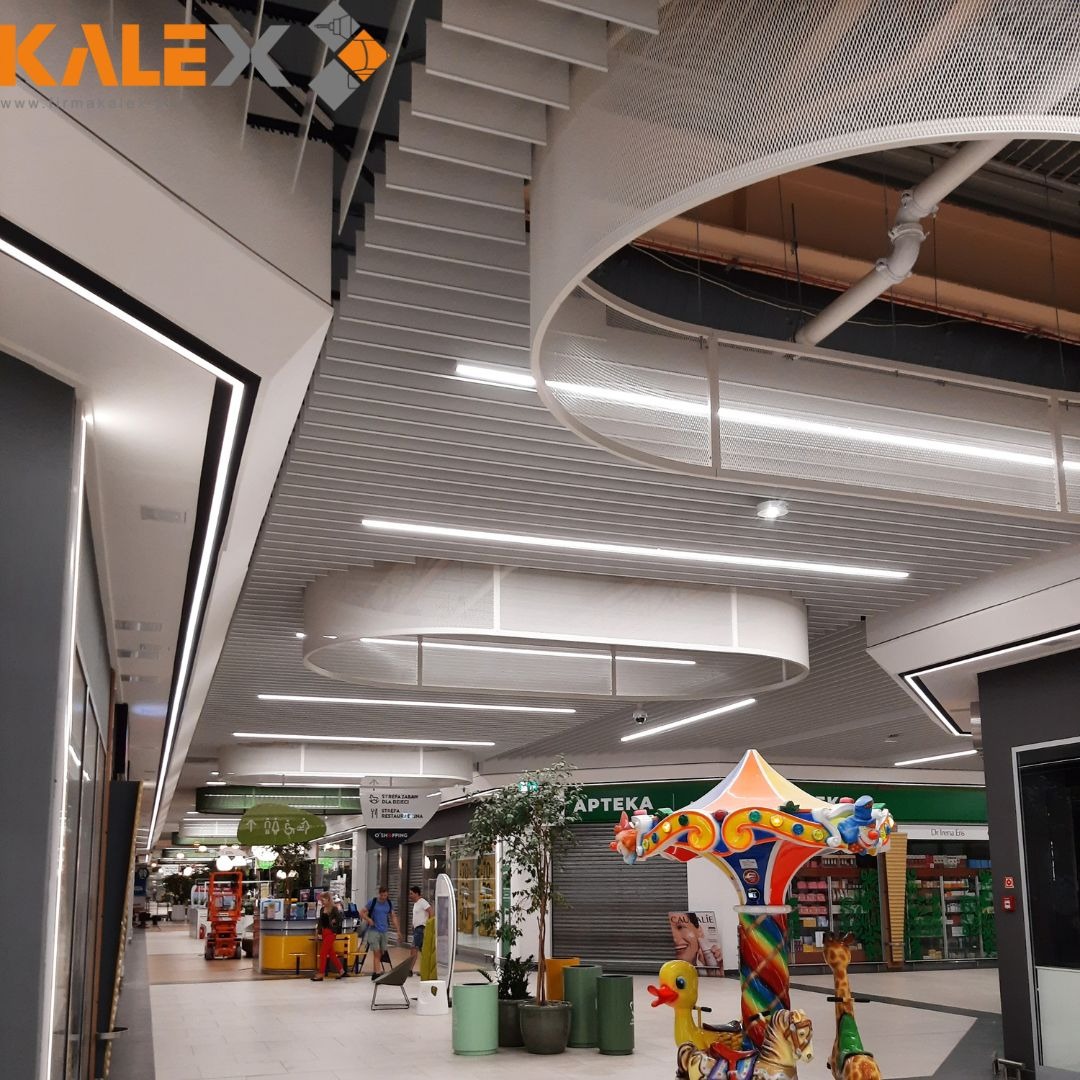 Sufit rastrowy z oświetleniem liniowym w pasażu handlowym, widoczne elementy dekoracyjne i karuzela dziecięca