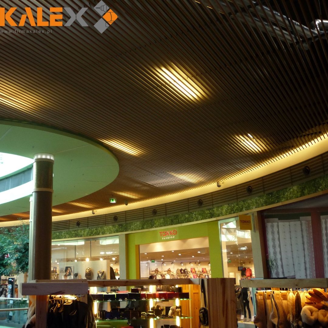 Drewniany sufit listwowy z oświetleniem w centrum handlowym, widok z dołu na zakrzywioną konstrukcję.