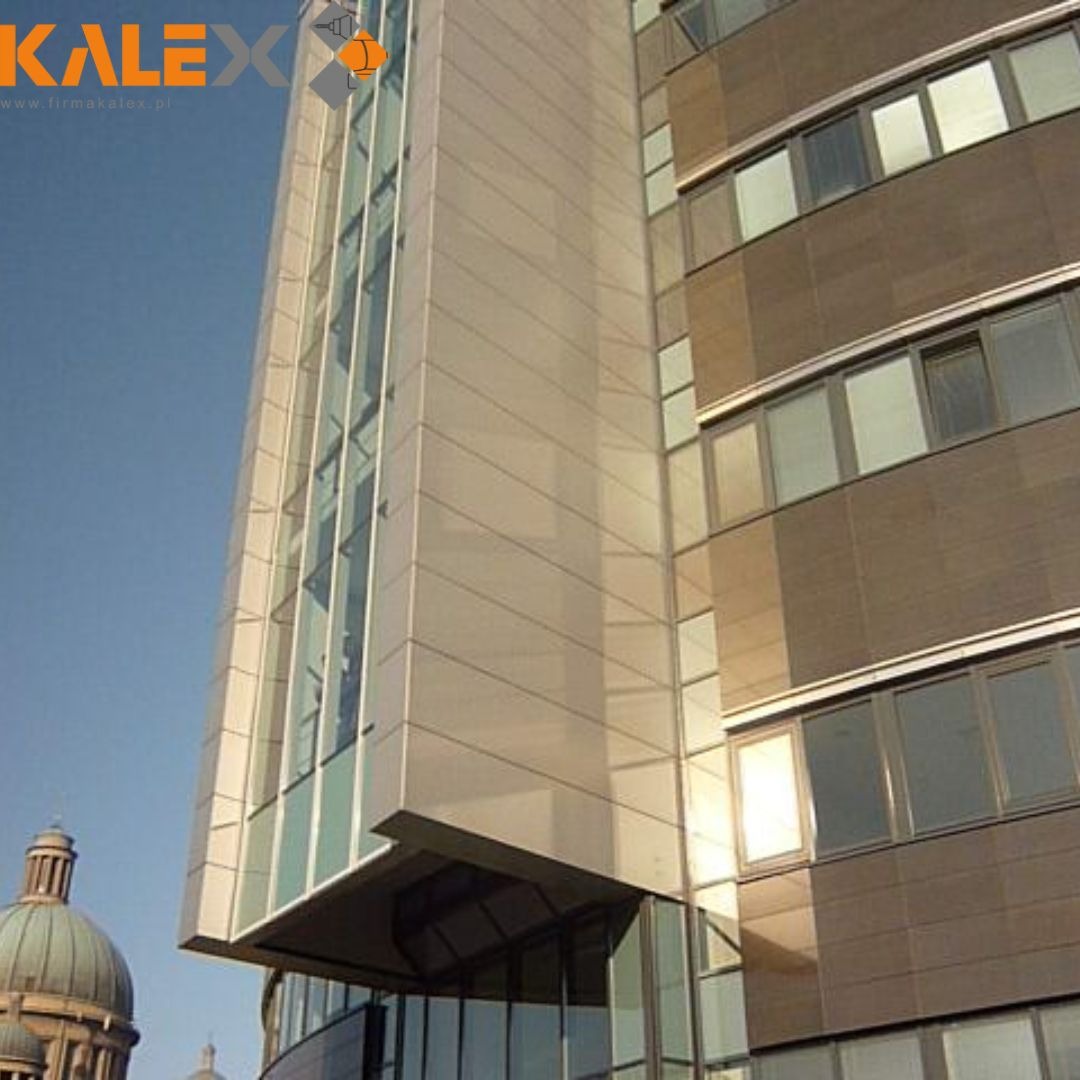 Elewacja biurowca z panelami w odcieniach szarości i brązu, z widocznym fragmentem zabytkowej kopuły w tle.