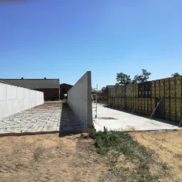 Budowa fundamentów budynku: widok na szalunki i zbrojenie, przygotowane do zalania betonem, z budynkami w tle.