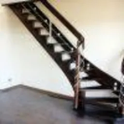 Ciemnobrązowe schody drewniane ze srebrną balustradą, widoczne z dołu, z ciemną podłogą i jasnymi ścianami, w minimalistycznym wnętrzu.