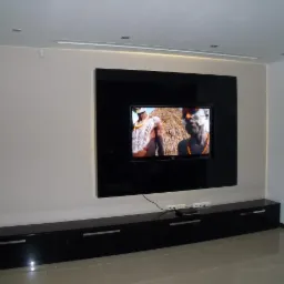 Nowoczesna zabudowa TV z czarnym, lakierowanym panelem na ścianie i szafką RTV z podłużnymi uchwytami. Minimalistyczny design i eleganckie wykończenie.