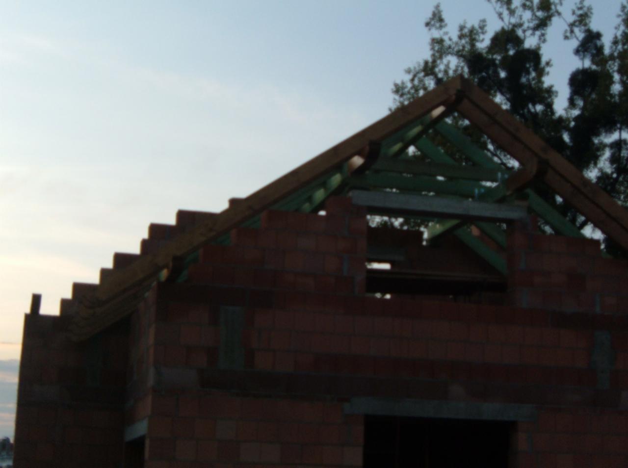 Wznoszenie murów z czerwonej cegły i konstrukcji drewnianej dachu w trakcie budowy domu jednorodzinnego, widok z dołu na tle nieba.