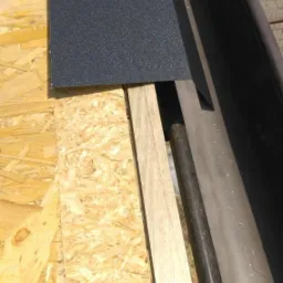 Fragment dachu z deskami OSB, papą bitumiczną i fragmentem rynny, widoczne elementy konstrukcyjne.