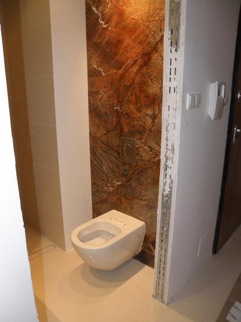 Podwieszana toaleta w łazience z marmurową ścianą i elementami wykończeniowymi w trakcie montażu.