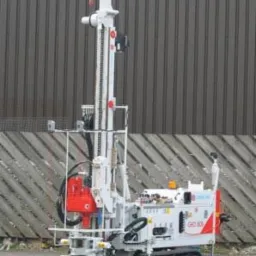 Mobilna wiertnica geologiczna na gąsienicach, model GEO 200, na tle szarej ściany z blachy trapezowej.