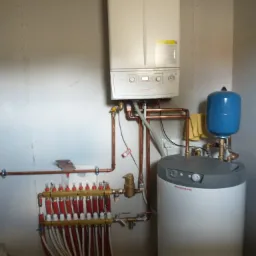 Kocioł gazowy Immergas z szarym zasobnikiem ciepłej wody i niebieskim naczyniem przeponowym, podłączony miedzianymi rurami do rozdzielacza ogrzewania podłogowego z czerwonymi zaworami.