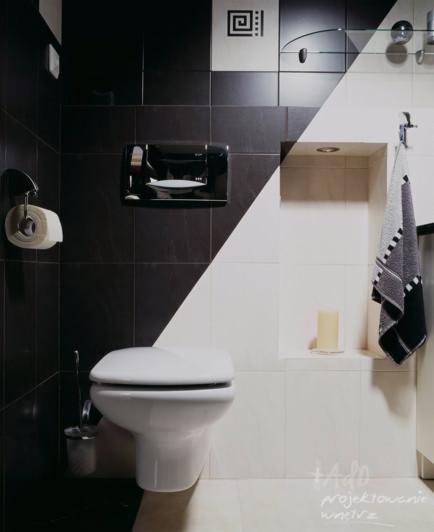 Nowoczesna toaleta w łazience z czarno-białymi płytkami ułożonymi po przekątnej, wisząca miska WC, minimalistyczny dozownik mydła i ręcznik w kontrastowych kolorach.