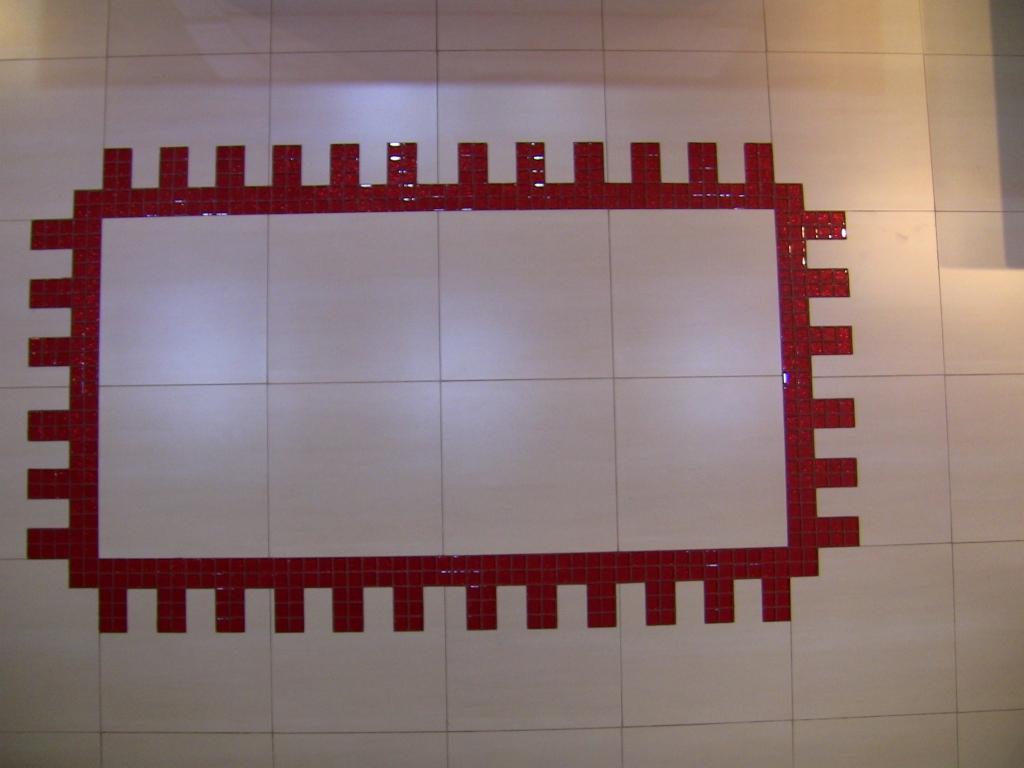 Wykończona ściana z jasnych płytek z dekoracyjnym obramowaniem z czerwonej mozaiki w kształcie stylizowanego zamku.