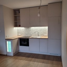 PPUH JAR DREW - Jasna kuchnia na wymiar z drewnianym blatem i mozaiką nad zlewem. Widoczne oświetlenie podszafkowe i wisząca żarówka. Podłoga z paneli imitujących drewno.