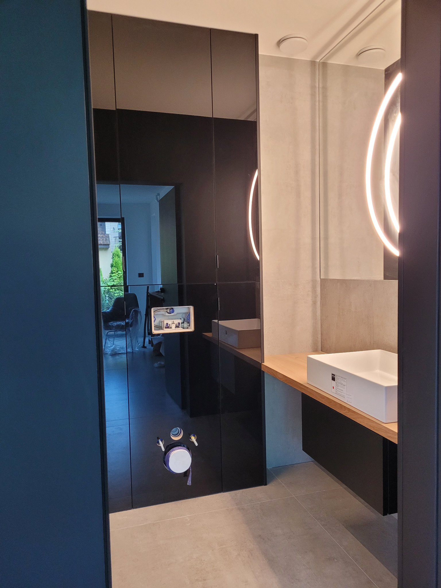 Nowoczesna łazienka z czarnymi, lustrzanymi drzwiami przesuwnymi, odbijającymi wnętrze domu. Umywalka nablatowa z oświetleniem LED w lustrze.