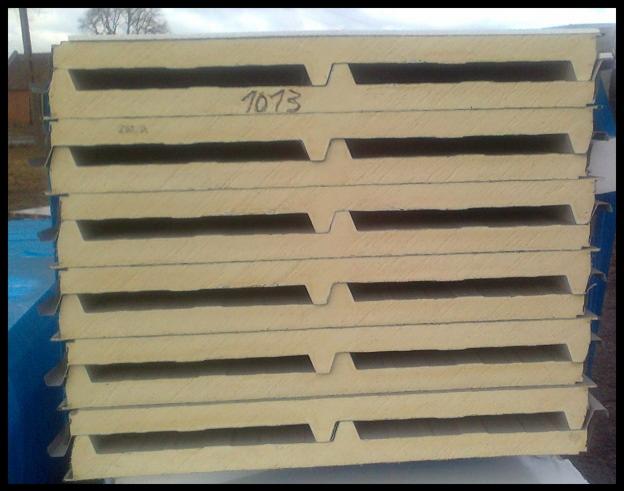 Stos płyt warstwowych dachowych z widocznym numerem '1073' napisanym odręcznie na jednej z płyt, ułożonych na niebieskiej plandece w plenerze.