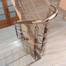 Klatka schodowa z marmurowymi stopniami i balustradą ze stali nierdzewnej z drewnianymi elementami, widok z góry na zakręt schodów.