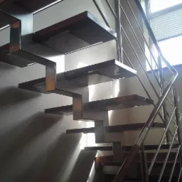 Nowoczesne schody z drewnianymi stopniami i metalową konstrukcją wspornikową oraz balustradą ze stali nierdzewnej, oświetlone od dołu, zrealizowane w Krępie.