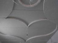 Sufit z płyt kartonowo-gipsowych z dekoracyjnymi, okrągłymi i falistymi elementami, widoczne przewody elektryczne, szpachlowane łączenia.