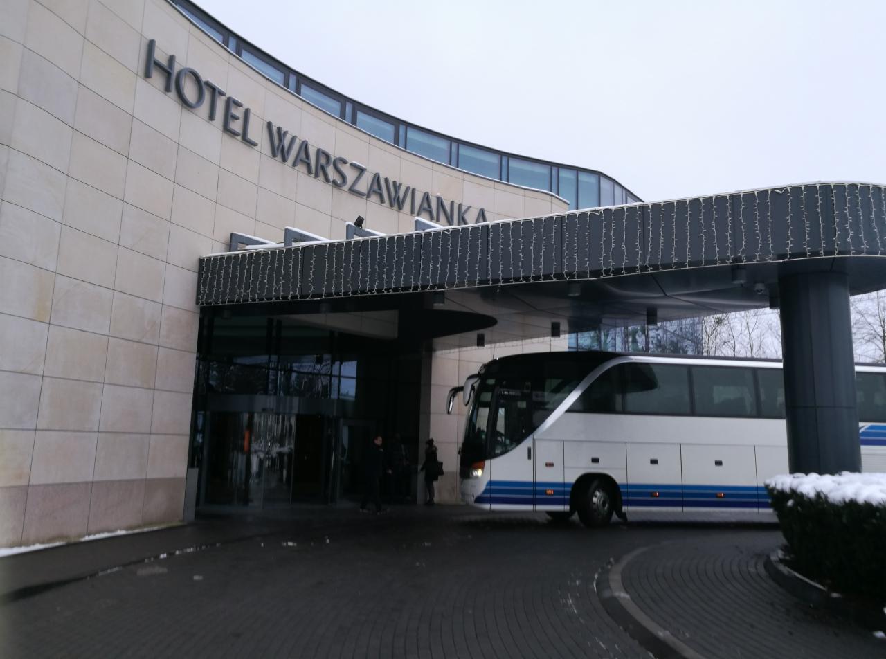 Biały autokar turystyczny parkuje pod zadaszonym wejściem do Hotelu Warszawianka, zimowy krajobraz.