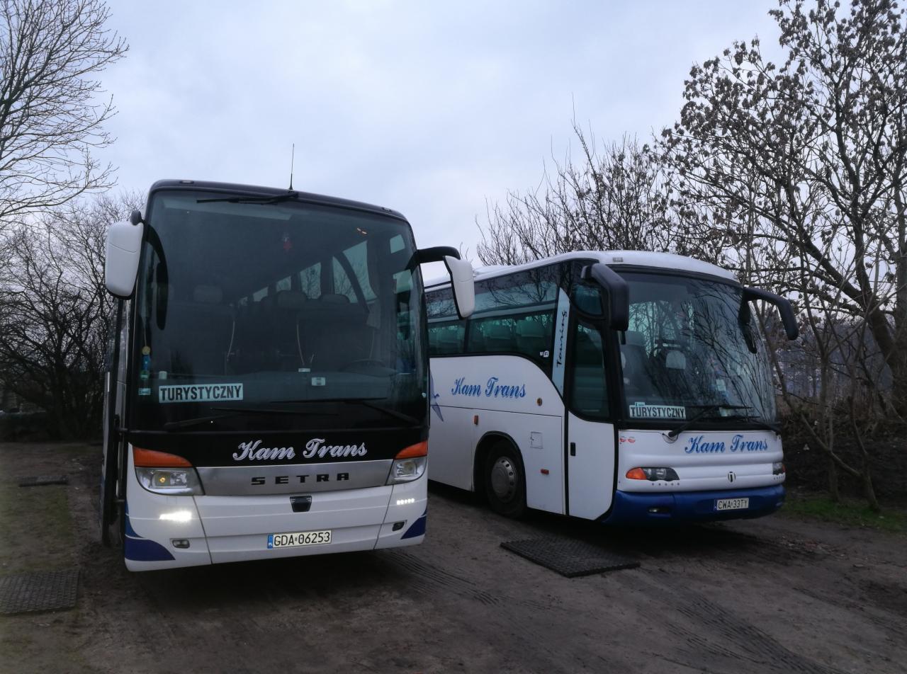 Dwa autokary firmy Kam Trans zaparkowane obok siebie na ziemistym placu, jeden czarno-biały z tablicą rejestracyjną GDA-06253, drugi biało-niebieski z tablicą CWA-33TY.