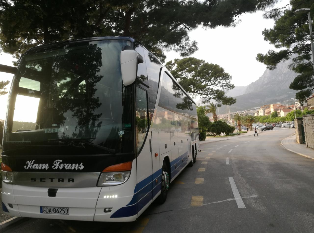 Autokar firmy Kam Trans marki Setra zaparkowany przy ulicy w miejscowości turystycznej z widokiem na góry.