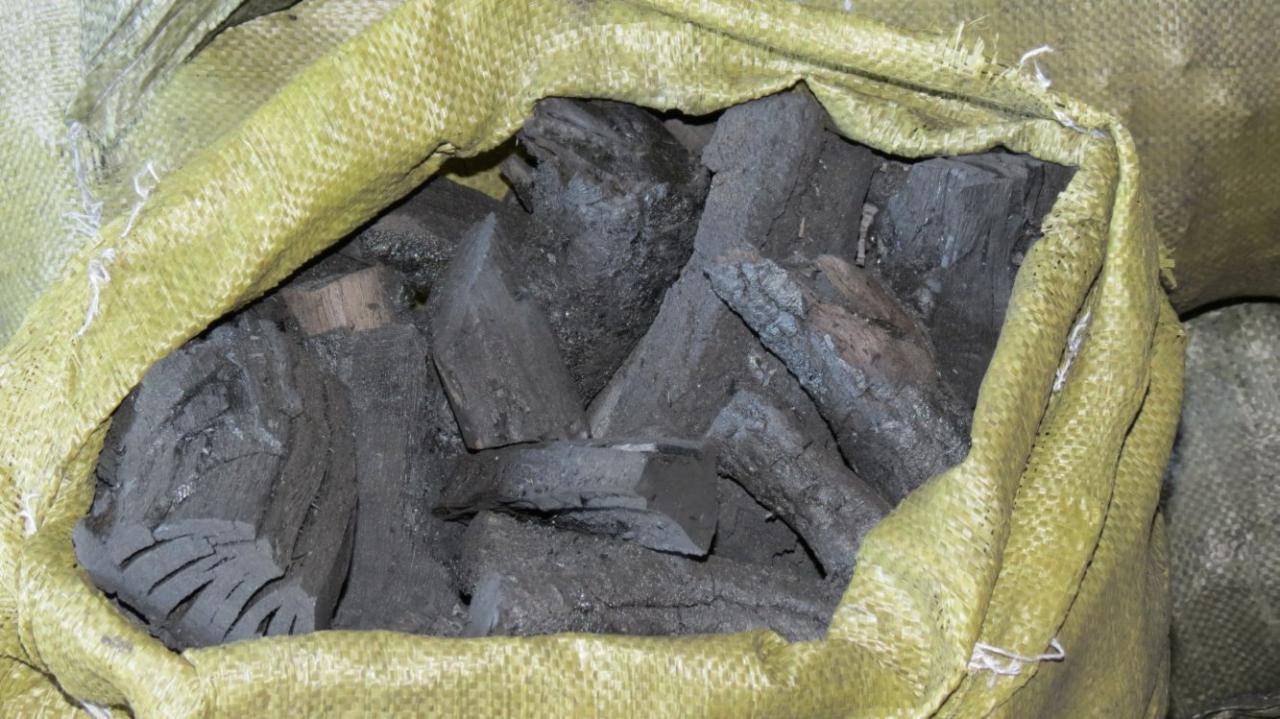 Worek jutowy wypełniony brykietami węgla drzewnego o nieregularnych kształtach i szarej barwie, widoczne fragmenty struktury drewna.