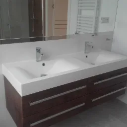 Nowoczesna łazienka z podwójną białą umywalką nablatową na szafce z ciemnego drewna i chromowanymi uchwytami, widok na lustro z odbiciem kabiny prysznicowej i grzejnika drabinkowego.