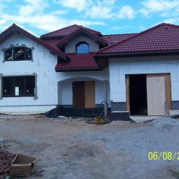 Eurobud - Surowy stan nowo budowanego domu z czerwonym dachem, widoczne bloczki z białego betonu komórkowego, niezabezpieczone okna, teren budowy z piaskiem i narzędziami, data na zdjęciu 06/08/2009.