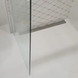 Nowoczesna kabina prysznicowa walk-in z odpływem liniowym, białe płytki podłogowe i ściana z mozaiką w romby.