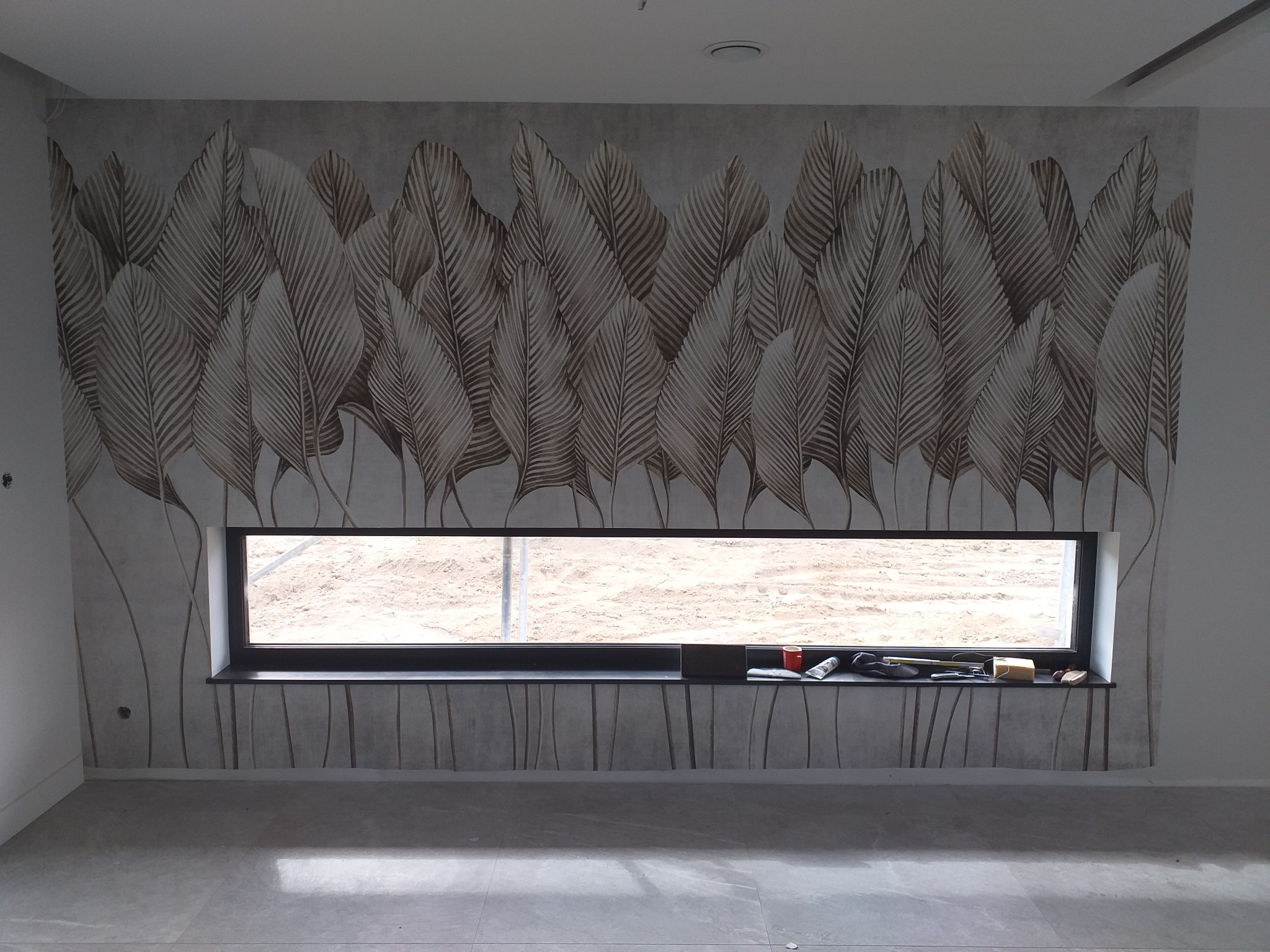 Ściana z tapetą w motywie liści palmowych, nad oknem narzędzia i akcesoria do tapetowania.