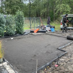 Garden Art Katarzyna Klimkowska - Przygotowany teren pod trawnik z rolki, obrzeża ułożone, widoczny pracownik i narzędzia. W tle drzewa i samochód dostawczy.